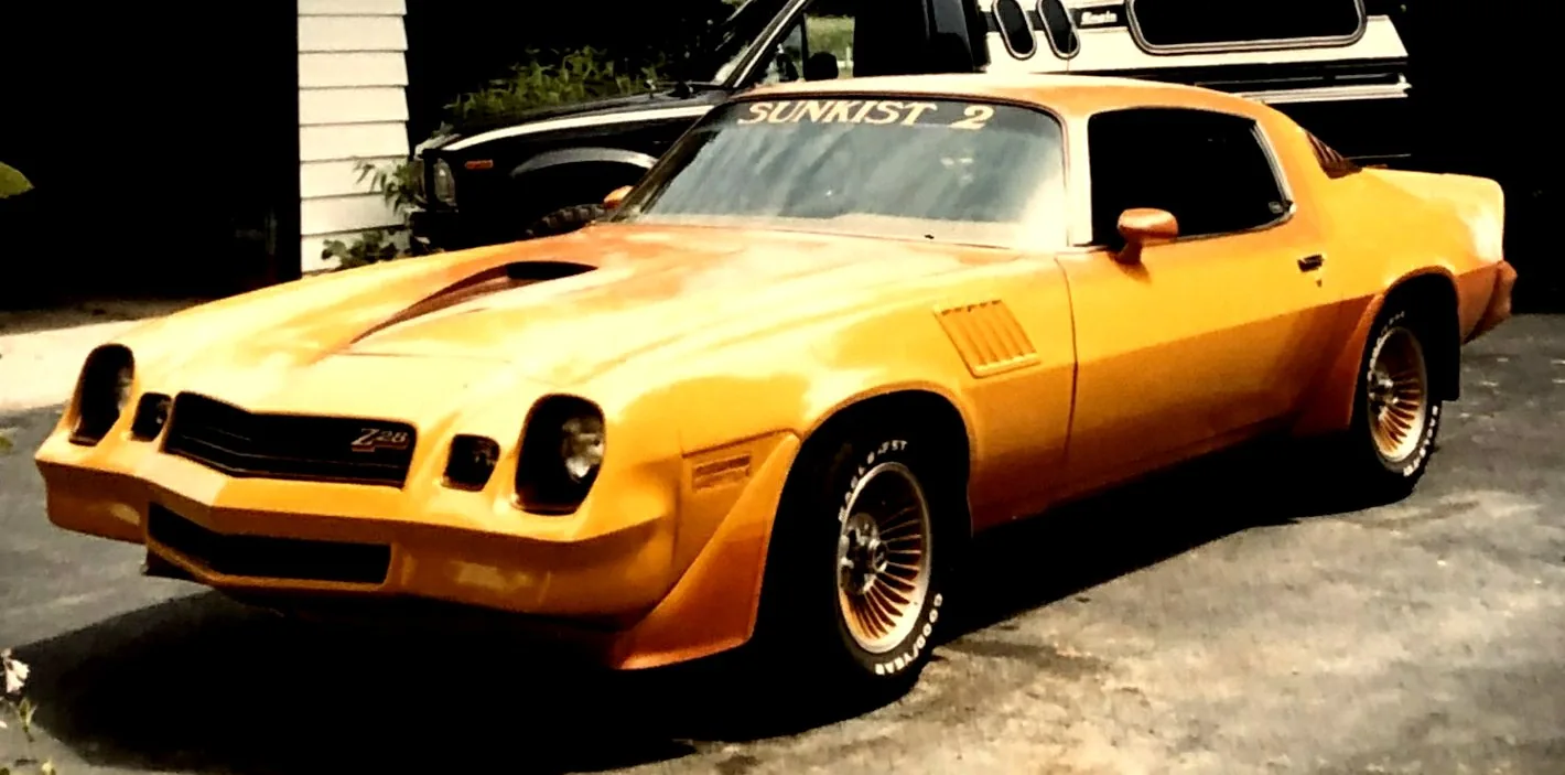 The owner's 1979-81 Chevy Camaro Z28 with a hand-done yellow-to-orange fade paint job, SUNKIST 2 windshield banner, black hood scoop and gold wire wheels on Goodyear white-letter tires